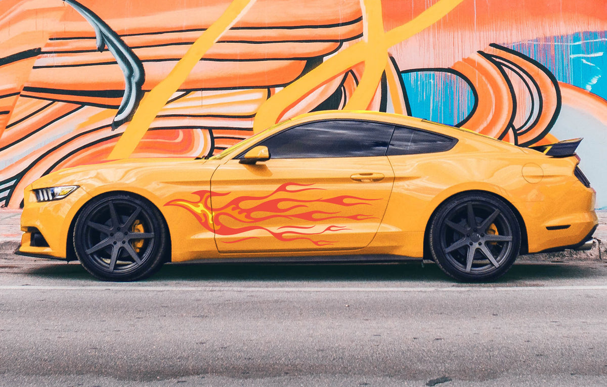 A bright yellow sports car with a retro hotrod look, complete with Cover-Alls' Endless Hotrod Flame Decal Kit on the side, is parked beside a colorful graffiti wall on the street.
