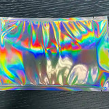 A sealed, iridescent foil packet with a rainbow-like sheen, crafted from easy-peel material, containing the Stickeeze Kid's Sticker Subscription Club by Stickeeze, placed on a dark, textured surface.