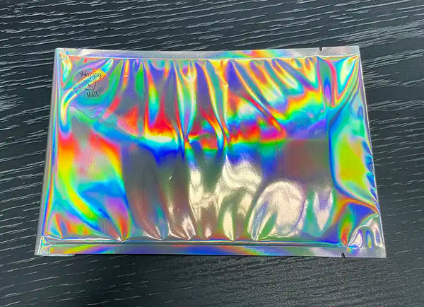 A sealed, iridescent foil packet with a rainbow-like sheen, crafted from easy-peel material, containing the Stickeeze Kid's Sticker Subscription Club by Stickeeze, placed on a dark, textured surface.