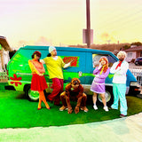 Five people in colorful costumes pose by a green and blue van decorated with Cover-Alls’ Mystery Machine Kit, bringing to life the classic Scooby-Doo cartoon characters.