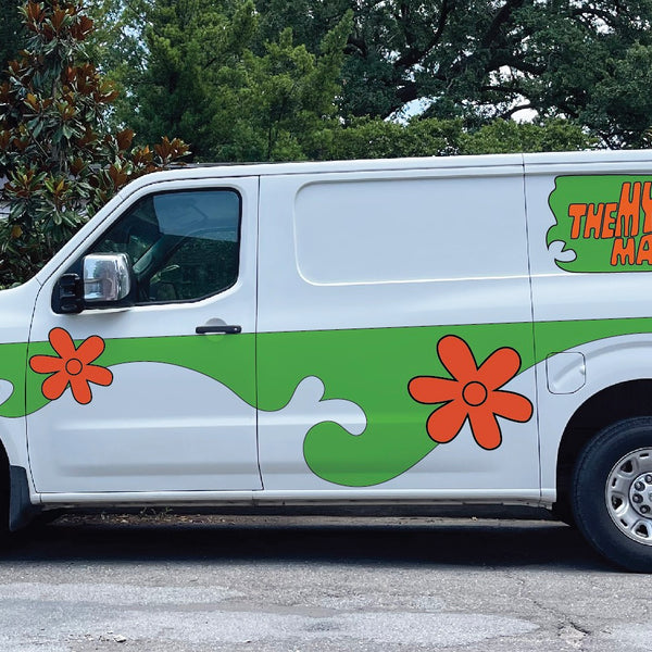 A white van with green and orange floral designs and the text "The Mystery Machine" on the side, reminiscent of Scooby Doo's iconic ride, parked on a street with trees in the background had just been fitted with a Cover-Alls Mystery Machine Kit.