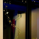 The window is adorned with reusable Gold Twinkly Stars from Cover-Alls, arranged in a spiral pattern. The room beyond the window has a subtle, dim light.