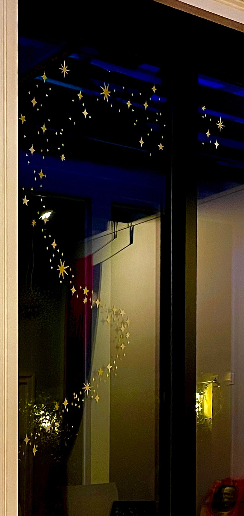 The window is adorned with reusable Gold Twinkly Stars from Cover-Alls, arranged in a spiral pattern. The room beyond the window has a subtle, dim light.