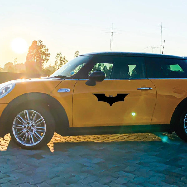 A yellow mini cooper with a Cover-Alls Bat hero symbol logo on the door, parked outdoors at sunset.