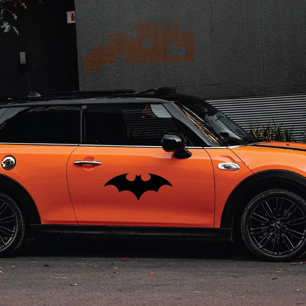 Orange mini cooper with a Cover-Alls Bat superhero symbol logo on the side parked on a street.