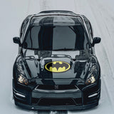 A black car with a Cover-Alls Bat superhero symbol logo on the hood, driving on a snowy road.