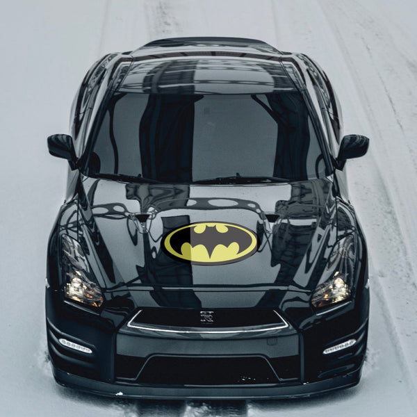 A black car with a Cover-Alls Bat superhero symbol logo on the hood, driving on a snowy road.