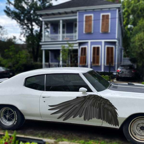 A white vintage car with large Cover-Alls black wings attached to the side, parked in front of a two-story purple house with greenery around.