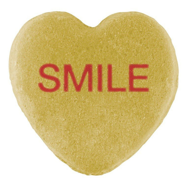 A heart-shaped sugar cookie with the word "smile" written in red icing and Cover-Alls candy hearts centered on top.