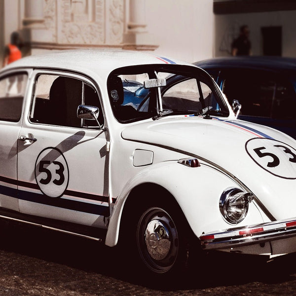 A classic Volkswagen Beetle painted white with blue and red VW bug stripes and the number 53 on its side, reminiscent of the iconic Herbie car with Cover-Alls Herbie the Race Car Decals.