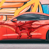 A red sports car with a Cover-Alls Red Dragon decal on the side, parked in front of a colorful, abstract graffiti wall.