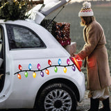 Dressed in a snug coat, someone arranges gift boxes in the trunk of a white car decorated with Cover-Alls' Christmas Lights Decals, spreading holiday cheer.