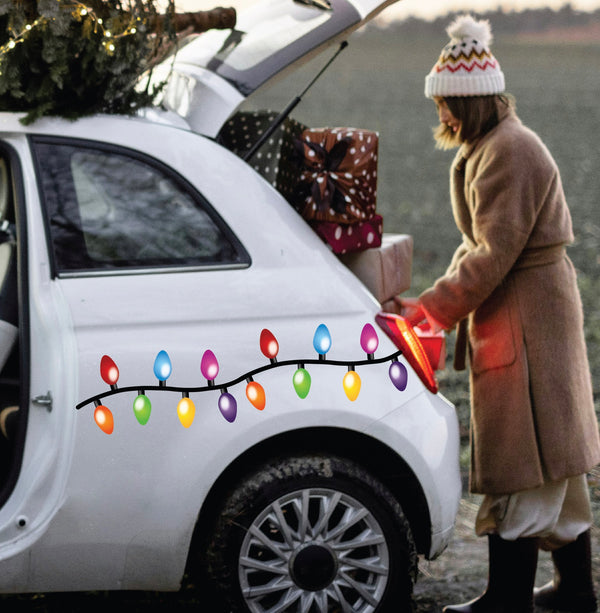 Dressed in a snug coat, someone arranges gift boxes in the trunk of a white car decorated with Cover-Alls' Christmas Lights Decals, spreading holiday cheer.