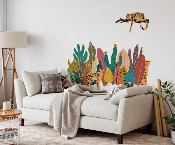 A modern living room featuring a beige sofa with a gray throw blanket, decorative cushions, and vibrant Boho Leopard Collection wall decals including leopards and simplified leaves by Cover-Alls.