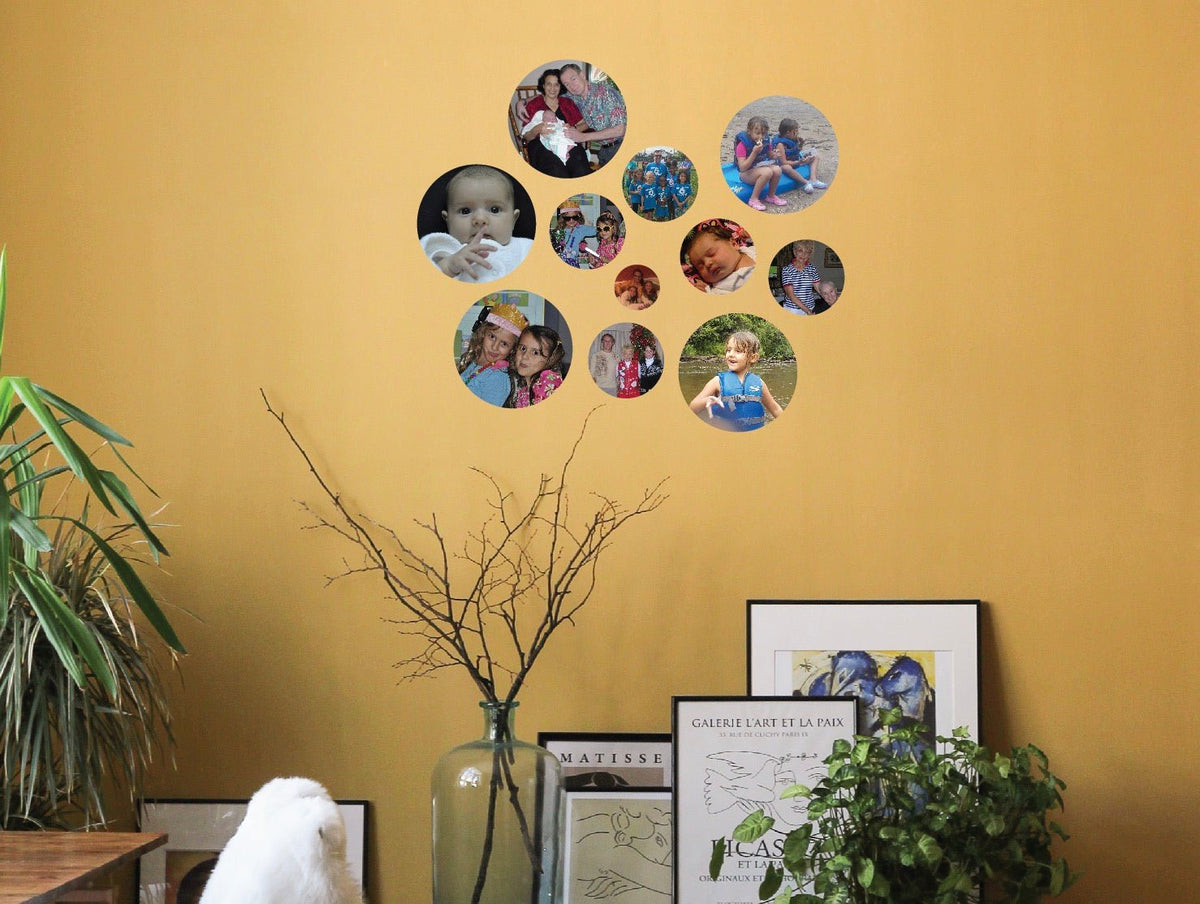 Collection of Cover-Alls Custom Photo Circle Decals on a mustard-colored photo wall, displaying diverse personal photos, above assorted framed art prints and plants in a cozy interior.