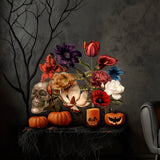 A still life composition featuring a skull, pumpkins, and a variety of colorful blooms is set on a table adorned with cobwebs against a dark, textured wall. Adding to the Halloween atmosphere is a black, leafless tree branch. This arrangement evokes an Old Master still life aesthetic and is perfectly complemented by Cover-Alls' Dark Romance Vintage Flower Decals.