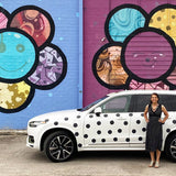 A woman standing beside a white SUV parked in front of a vibrant mural featuring large, colorful Cover-Alls Dot Decals on a purple wall.