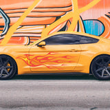 A bright yellow sports car with a retro hotrod look, complete with Cover-Alls' Endless Hotrod Flame Decal Kit on the side, is parked beside a colorful graffiti wall on the street.
