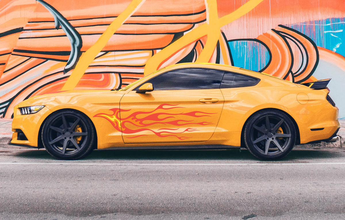 A bright yellow sports car with a retro hotrod look, complete with Cover-Alls' Endless Hotrod Flame Decal Kit on the side, is parked beside a colorful graffiti wall on the street.