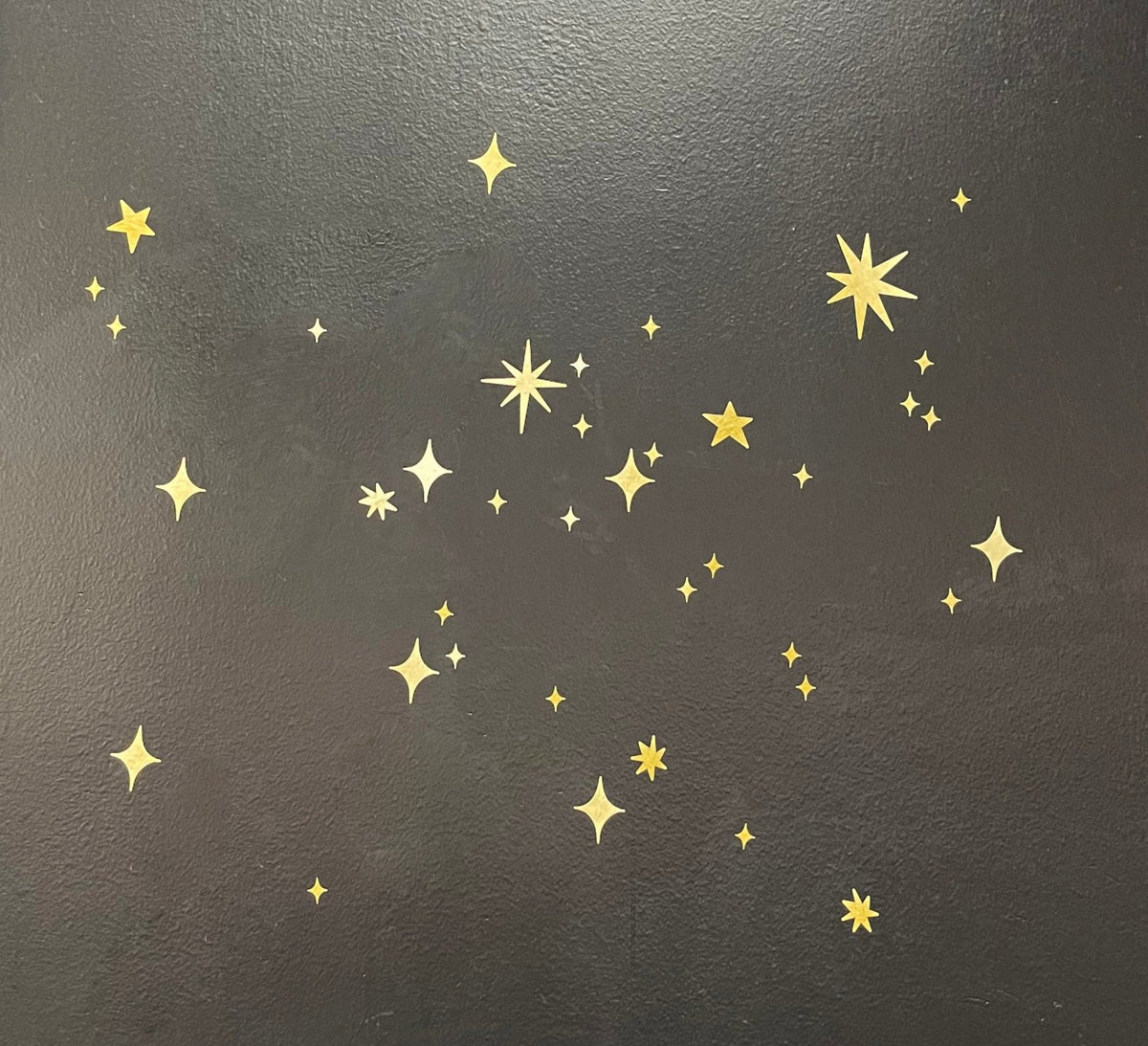 Gold Twinkly Stars stickers of various sizes scattered randomly on a dark gray background, creating a magical scene decor. (Cover-Alls)