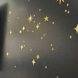 Gold Twinkly Stars stickers of various sizes and designs scattered on a dark textured surface, perfect for creating a magical scene decor. Brand Name: Cover-Alls