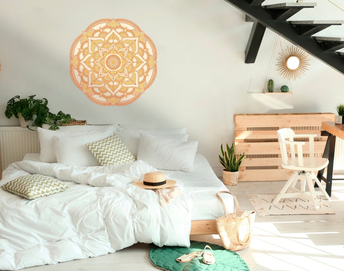Bright, airy bedroom with a white bed, decorative pillows, a straw hat on the bed, wooden furniture, plants, and Cover-Alls mandala wall decals.