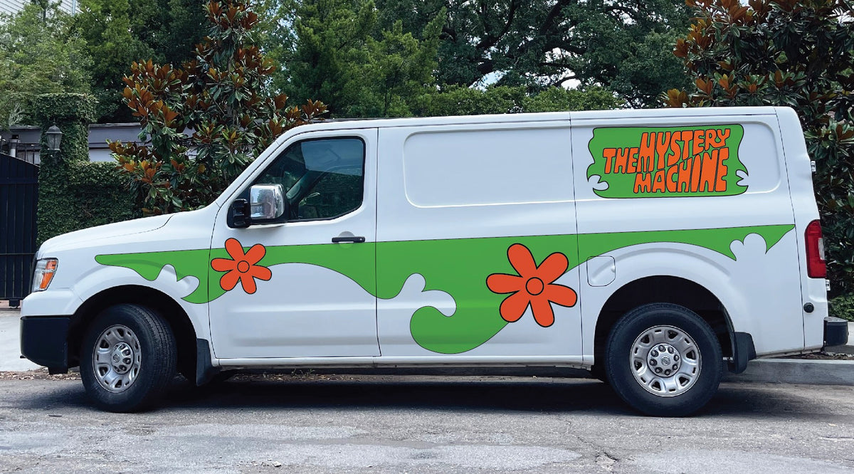 A white van with green and orange floral designs and the text "The Mystery Machine" on the side, reminiscent of Scooby Doo's iconic ride, parked on a street with trees in the background had just been fitted with a Cover-Alls Mystery Machine Kit.