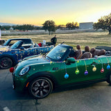 Two mini convertibles, decorated with Cover-Alls Christmas Ornament Ball Decals, adorn an open area at sunset.