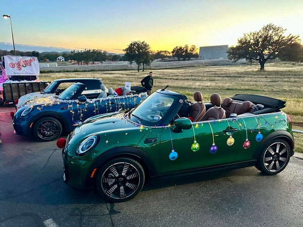 Two mini convertibles, decorated with Cover-Alls Christmas Ornament Ball Decals, adorn an open area at sunset.