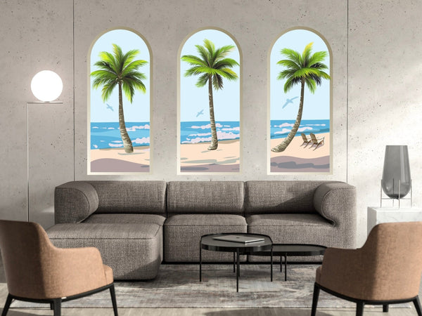 A modern living room with a gray sofa and two brown chairs facing each other, three framed beach wall decor paintings above the sofa, a round lamp, and a set of black coffee tables featuring Palm Tree Arch Scene Decals by Cover-Alls.
