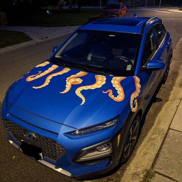 A blue car decked out with Cover-Alls' Eight Terrifying Tentacle Decals on its hood and front fenders is parked on the side of a suburban street at night.