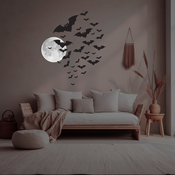 A cozy room with a sofa adorned with pillows and a blanket. The wall is decorated with the Cover-Alls' Cauldron of Bats Decals, showcasing realistic bat dimensions along with a moon. Decorative items like a pouf, wicker basket, and dried plants are scattered around, adding a touch of charm.