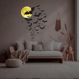 A cozy living room with a white sofa, beige throw blanket, and pillows. The wall features glowing moon decorations and **Cover-Alls' Cauldron of Bats Decals** in various sizes. The room is adorned with a pouf and dried plants.