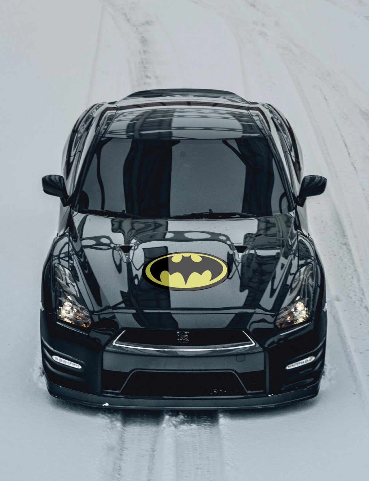 A black car with a Cover-Alls Bat superhero symbol logo on the hood, driving on a snowy road.
