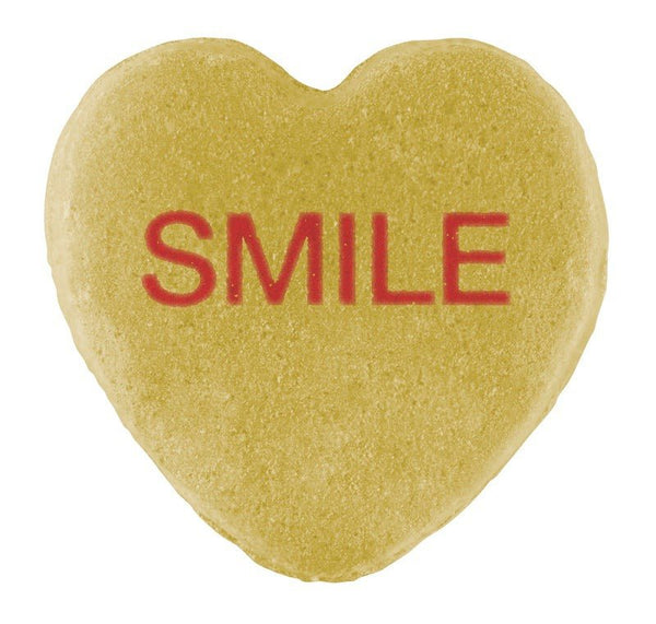 A heart-shaped sugar cookie with the word "smile" written in red icing and Cover-Alls candy hearts centered on top.