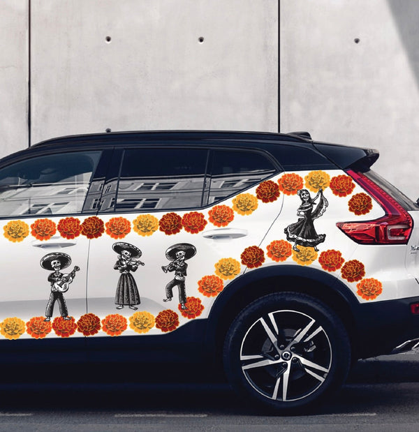 White Day of the Dead Mariachi Band SUV with colorful Dia de Los Muertos-themed decals, featuring sugar skulls and orange flowers, parked beside a gray wall. Brand name: Cover-Alls.