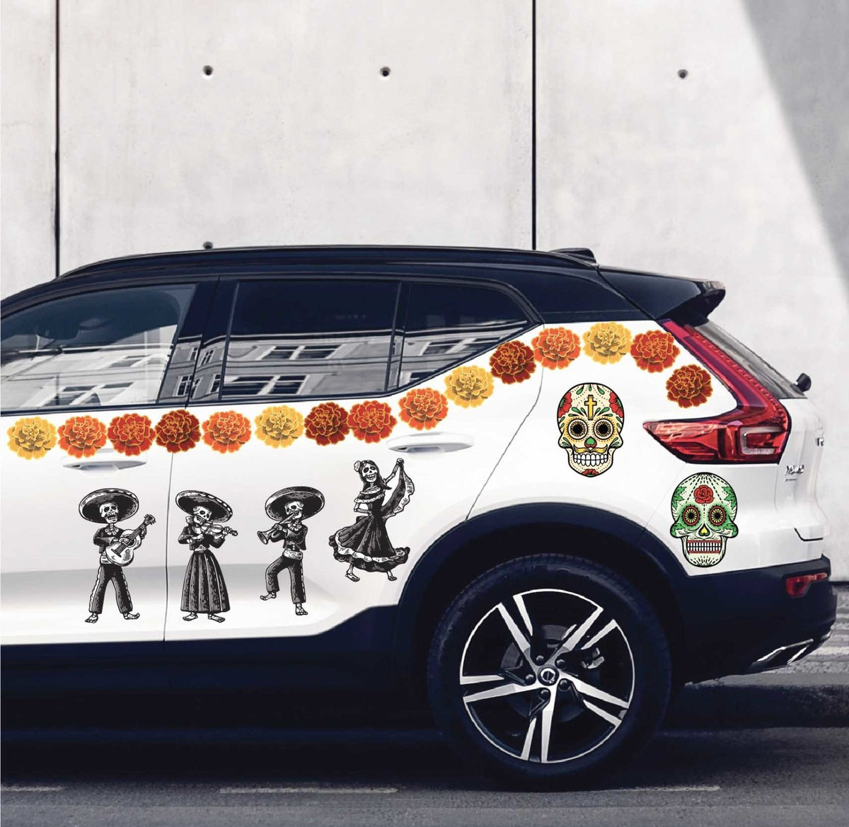 White SUV decorated with colorful Cover-Alls Day of the Dead Painted Skull Calaveras decals, including painted skull figures and flowers, parked by a white wall.