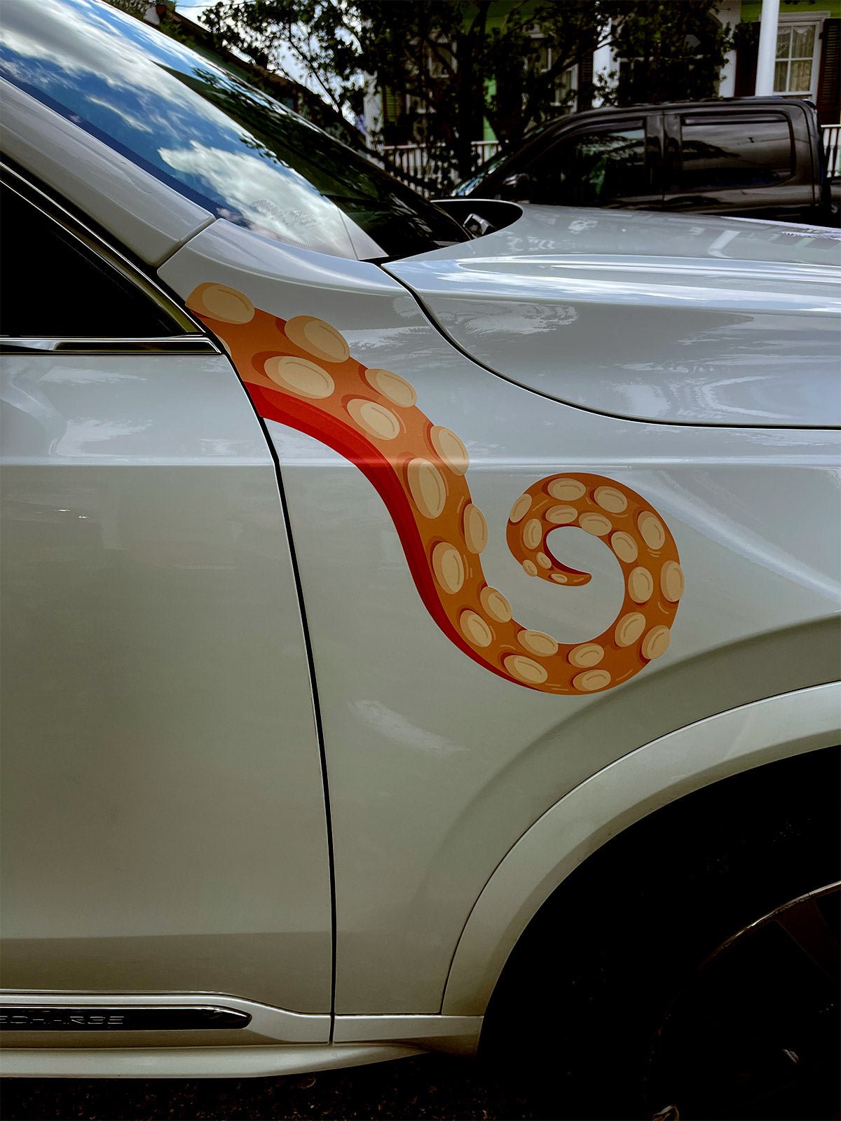 A silver car with Eight Terrifying Tentacle Decals by Cover-Alls, featuring a decorative red and orange giant squid tentacle design on the door, parked on a street.