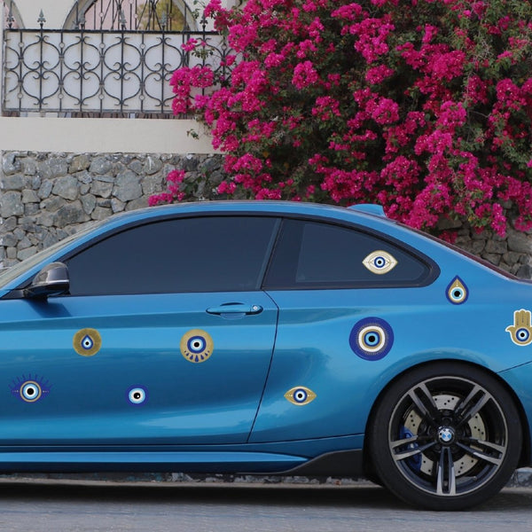 A vibrant blue car decorated with multiple Cover-Alls Evil Eye Decals parked beside a sidewalk with pink flowers and a stone wall in the background.