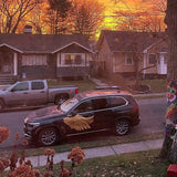 A sunset casts a warm glow over a suburban street, highlighting a car with Cover-Alls Gold Wing Decals parked next to tree-lined sidewalks.