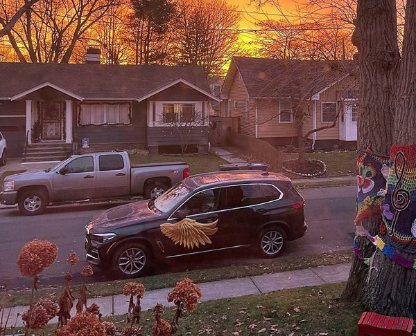 A sunset casts a warm glow over a suburban street, highlighting a car with Cover-Alls Gold Wing Decals parked next to tree-lined sidewalks.