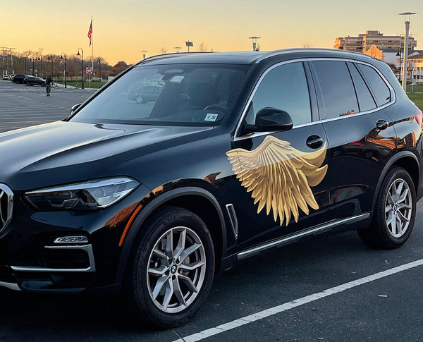 A black BMW SUV with large Cover-Alls Gold Wing Decals decoration on its front door, parked in a lot during sunset.