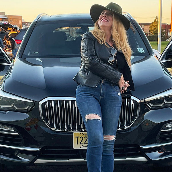 Woman in a black leather jacket and ripped jeans standing in front of a black SUV with Cover-Alls Gold Wing Decals for doors open.