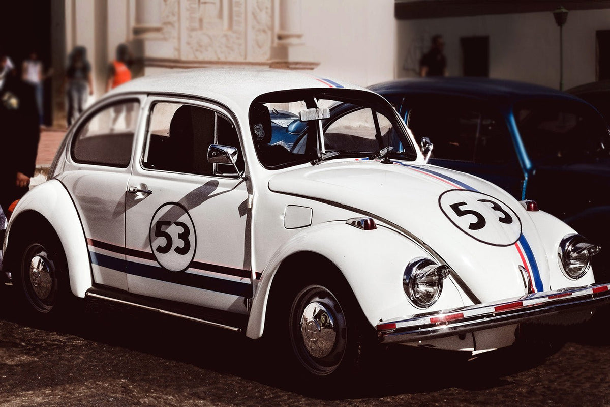 A classic Volkswagen Beetle painted white with blue and red VW bug stripes and the number 53 on its side, reminiscent of the iconic Herbie car with Cover-Alls Herbie the Race Car Decals.