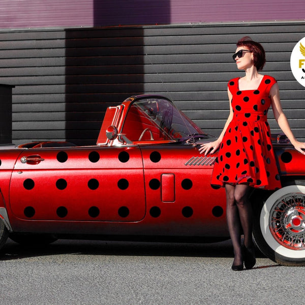 A woman in a red polka dot dress and sunglasses leaning on a red car with Cover-Alls Dot Decals, standing in front of a building.