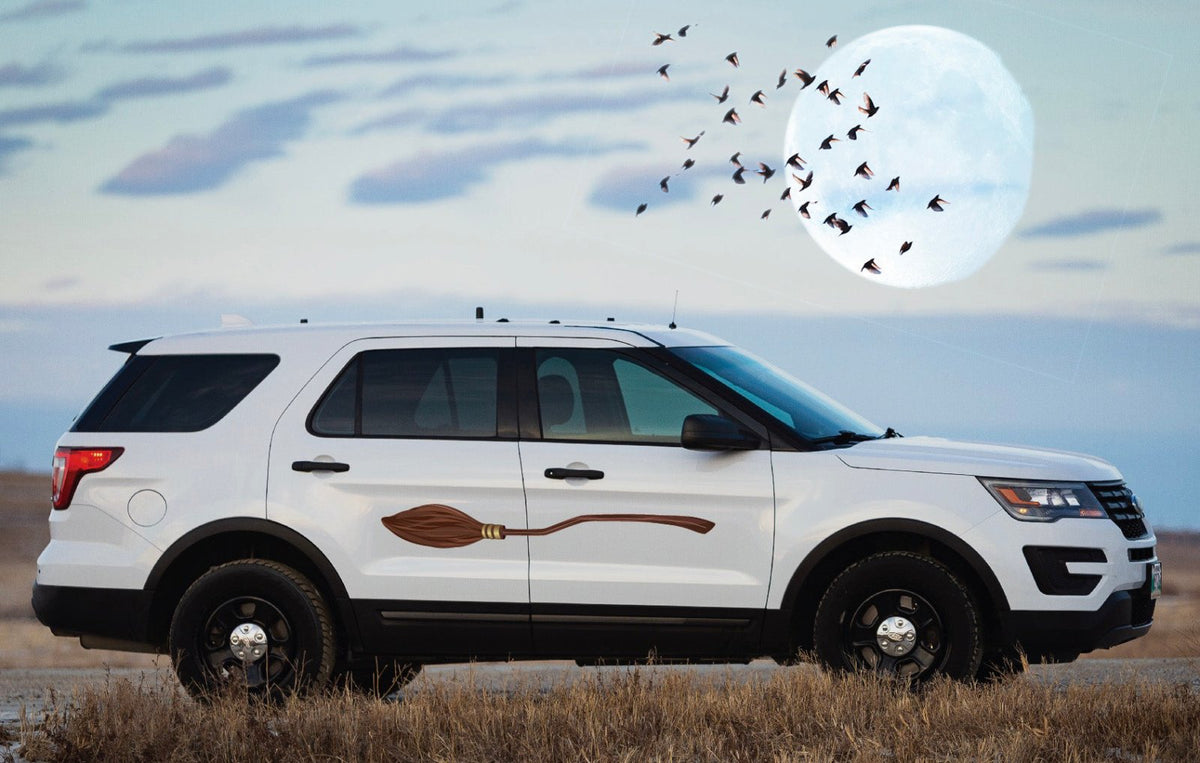 A white SUV with a Cover-Alls Magical Broomstick decal parked in a field under a full moon with birds flying in the background.