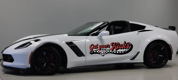White Chevrolet Corvette with black and red trim, featuring Cover-Alls Route 66 decals, parked in a showroom.