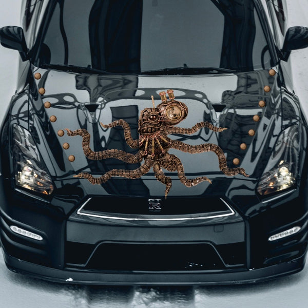 A large Cover-Alls Steampunk Octopus Decal in bronze hues rests on the hood of a glossy black car on a snowy day.