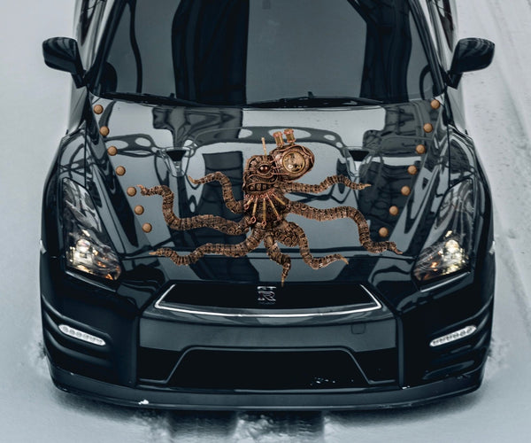 A large Cover-Alls Steampunk Octopus Decal in bronze hues rests on the hood of a glossy black car on a snowy day.