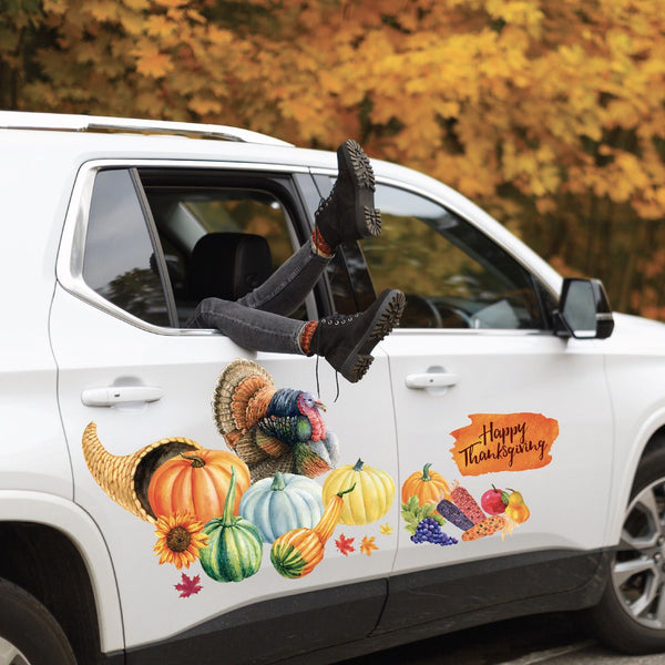 A white SUV with a person's legs and Cover-Alls Thanksgiving Cornucopia Decals sticking out of the window, parked beside trees with autumn leaves.